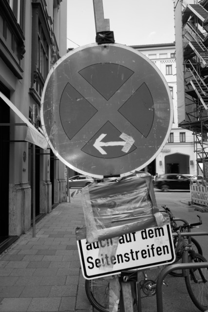 Verschiedene Straßenschilder, ein davon ist abgeklebt, schwarz-weiß